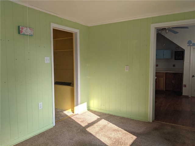 carpeted empty room featuring ceiling fan, wood walls, and ornamental molding