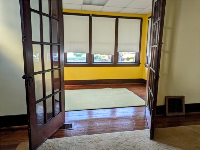 interior space featuring a drop ceiling, hardwood / wood-style floors, and french doors