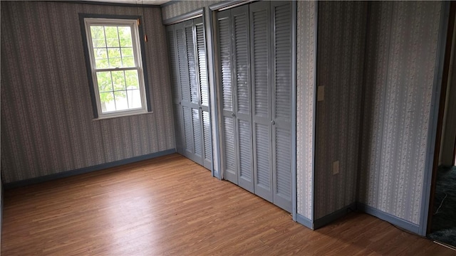 interior space with wallpapered walls, wood finished floors, and baseboards