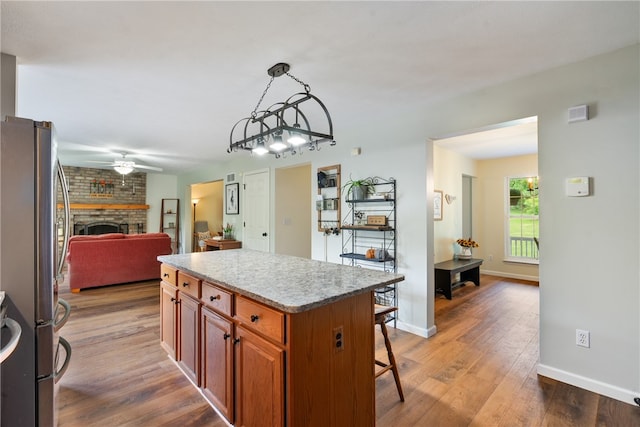 kitchen featuring dark wood-type flooring, a center island, stainless steel refrigerator, a fireplace, and decorative light fixtures