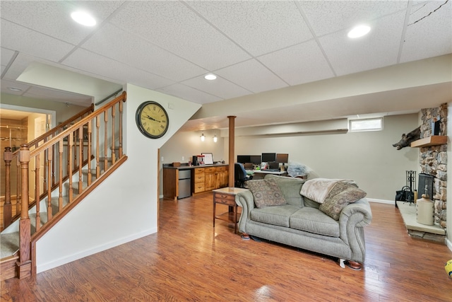 living room with a stone fireplace, a paneled ceiling, and hardwood / wood-style floors