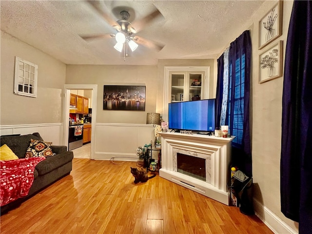 living room with ceiling fan, light hardwood / wood-style floors, and a textured ceiling