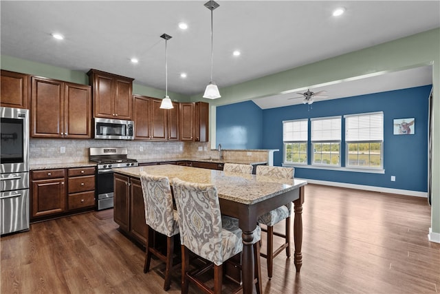 kitchen featuring a breakfast bar, dark hardwood / wood-style floors, appliances with stainless steel finishes, decorative light fixtures, and ceiling fan