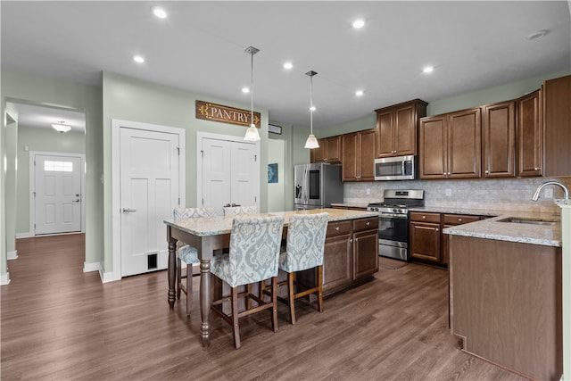 kitchen featuring appliances with stainless steel finishes, dark wood-type flooring, pendant lighting, a center island, and sink