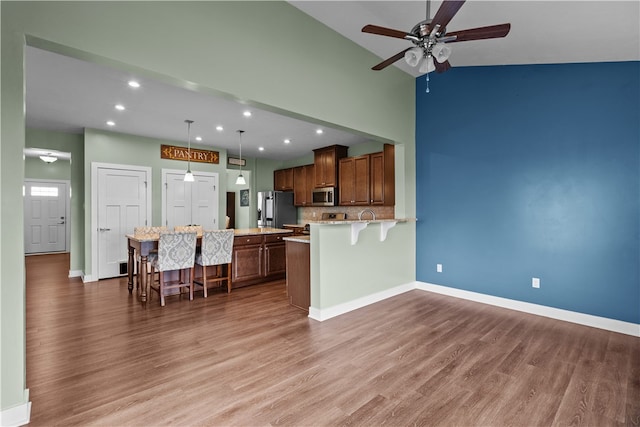 kitchen featuring a breakfast bar, hardwood / wood-style flooring, stainless steel appliances, decorative light fixtures, and ceiling fan