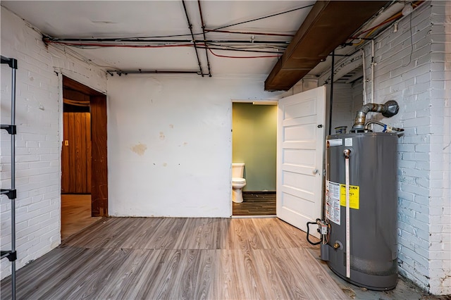 basement with brick wall, water heater, and light wood-type flooring