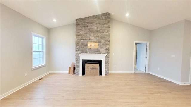 unfurnished living room with light wood-type flooring, vaulted ceiling, and a stone fireplace