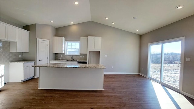 kitchen featuring decorative backsplash, a kitchen island, light stone countertops, and white cabinetry