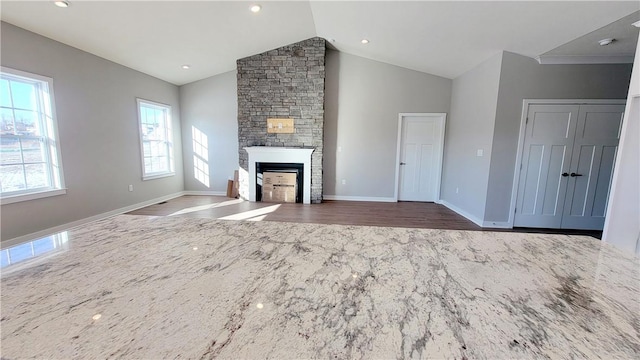 unfurnished living room with a stone fireplace, dark wood-type flooring, and vaulted ceiling