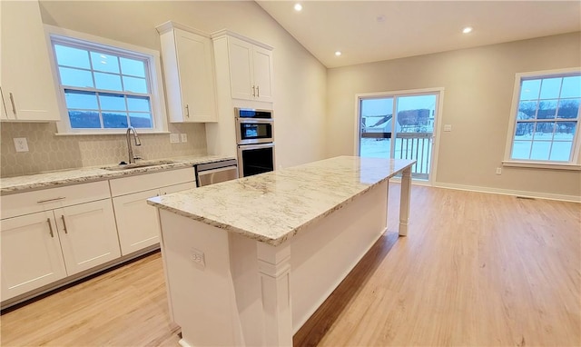 kitchen with white cabinetry, sink, light stone countertops, a kitchen island, and light wood-type flooring