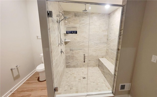 bathroom with hardwood / wood-style floors, toilet, and a shower with door