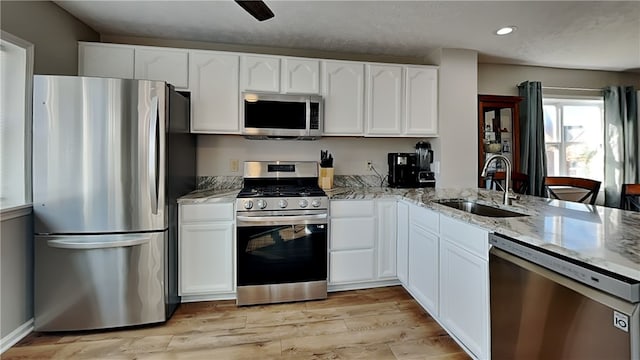 kitchen featuring stainless steel appliances, white cabinetry, sink, light stone counters, and light wood-type flooring