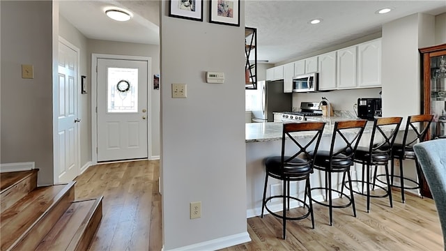 kitchen with light hardwood / wood-style floors, a breakfast bar, appliances with stainless steel finishes, kitchen peninsula, and white cabinets