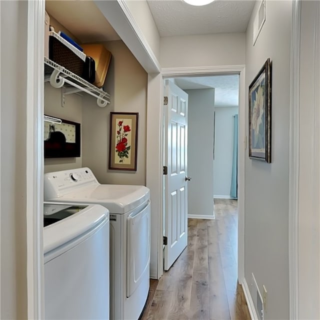 laundry area with washing machine and clothes dryer, a textured ceiling, and light wood-type flooring