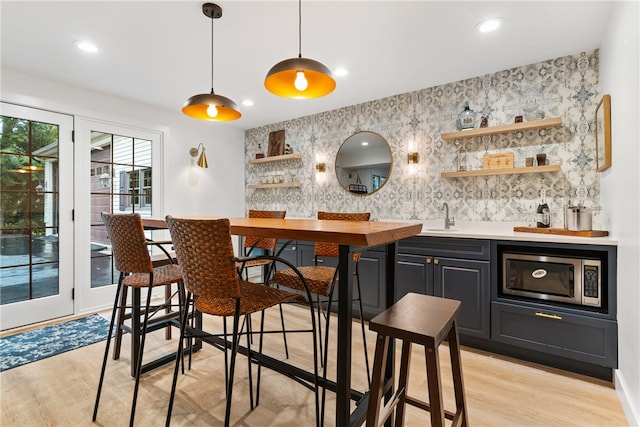 bar featuring pendant lighting, light wood-type flooring, stainless steel microwave, and sink