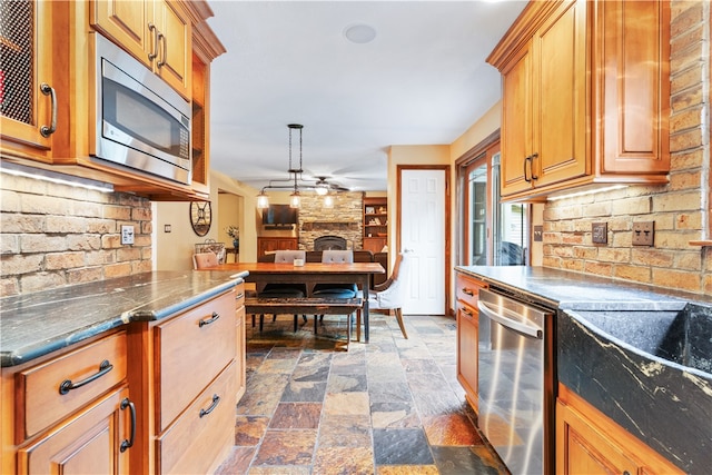 kitchen featuring appliances with stainless steel finishes, ceiling fan, backsplash, a fireplace, and pendant lighting