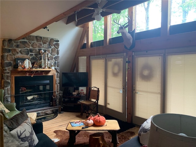 living room with hardwood / wood-style floors, ceiling fan, beamed ceiling, a high ceiling, and a stone fireplace