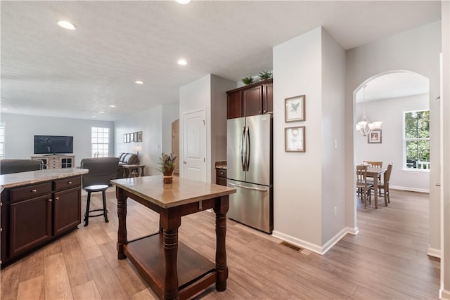 kitchen with a notable chandelier, dark brown cabinets, light wood-type flooring, and stainless steel refrigerator