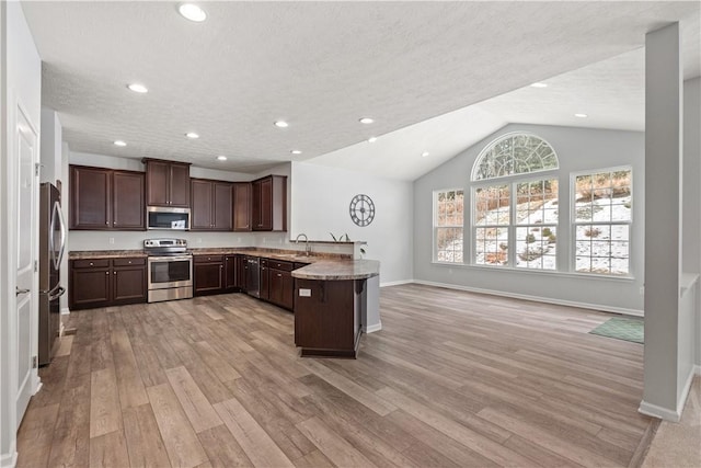 kitchen featuring light stone countertops, dark brown cabinetry, stainless steel appliances, vaulted ceiling, and light hardwood / wood-style flooring