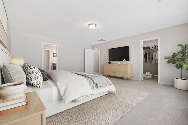 bedroom with ensuite bathroom, light colored carpet, a walk in closet, and a closet