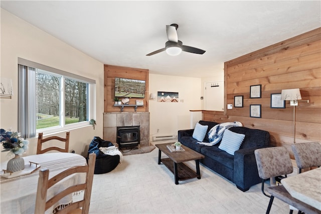 carpeted living room featuring ceiling fan, a wood stove, wooden walls, baseboard heating, and a fireplace