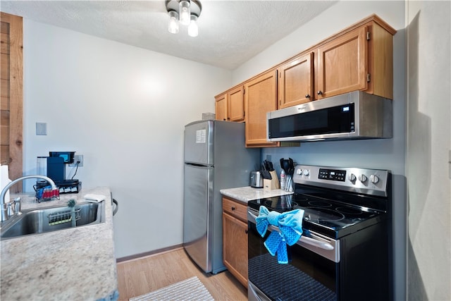 kitchen featuring appliances with stainless steel finishes, a textured ceiling, light wood-type flooring, and sink