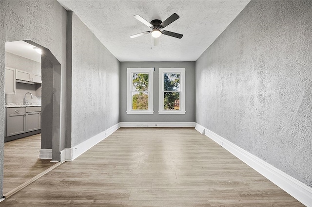 empty room featuring ceiling fan, a textured ceiling, light wood-type flooring, and sink