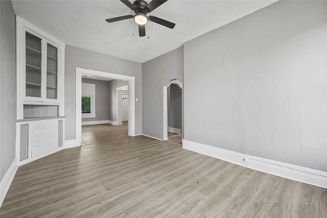 empty room featuring wood-type flooring, ceiling fan, built in shelves, and a textured ceiling