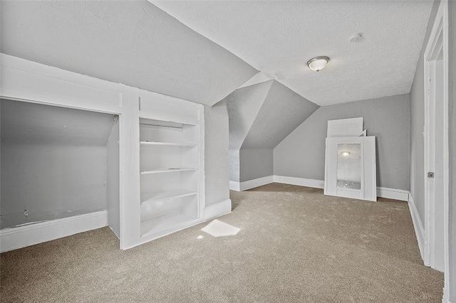 additional living space with a textured ceiling, built in shelves, carpet flooring, and vaulted ceiling