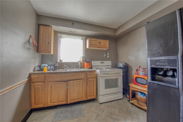 kitchen with light parquet flooring, sink, gas range gas stove, and stainless steel fridge