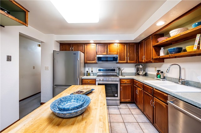 kitchen with light tile patterned floors, butcher block countertops, stainless steel appliances, and sink