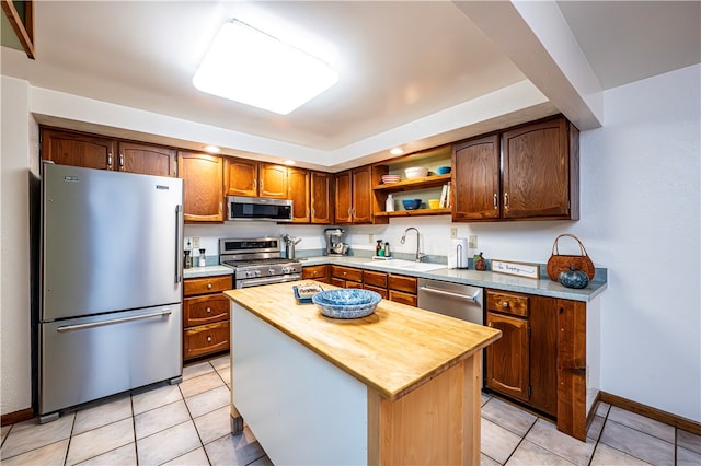 kitchen with light tile patterned flooring, sink, a kitchen island, stainless steel appliances, and butcher block counters