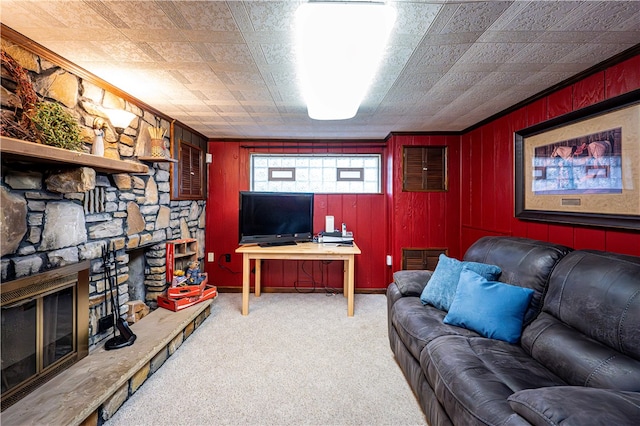 carpeted living room with a stone fireplace and wooden walls