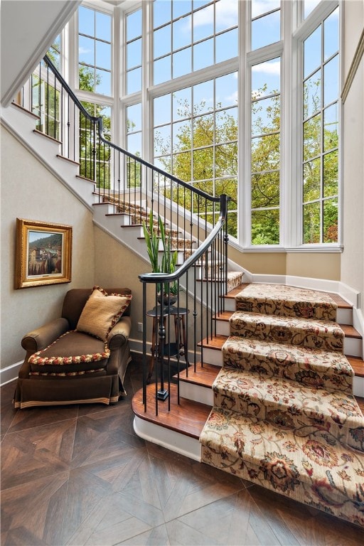 stairs with a towering ceiling, parquet flooring, and a wealth of natural light