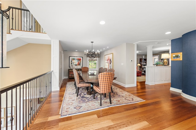 dining room featuring a notable chandelier, decorative columns, and hardwood / wood-style flooring