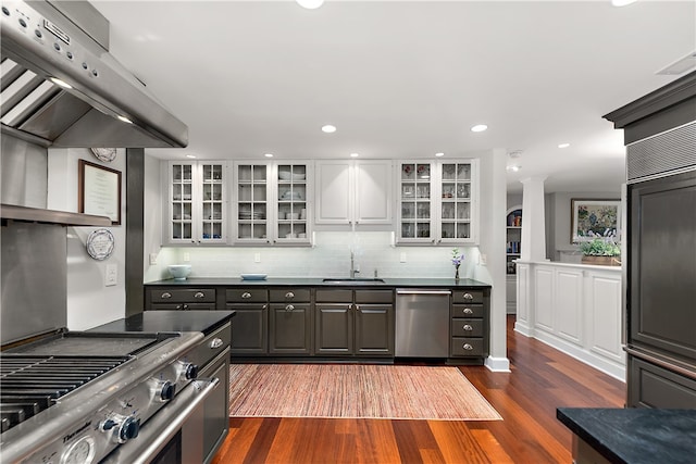 kitchen with appliances with stainless steel finishes, white cabinets, dark hardwood / wood-style floors, extractor fan, and sink