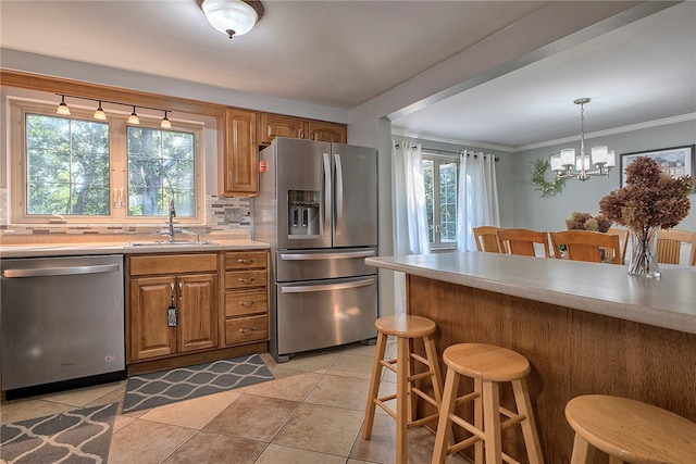 kitchen with appliances with stainless steel finishes, a healthy amount of sunlight, sink, and a notable chandelier