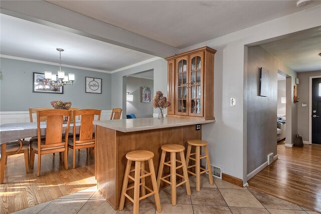 kitchen with light wood-type flooring, a chandelier, kitchen peninsula, a kitchen breakfast bar, and decorative light fixtures