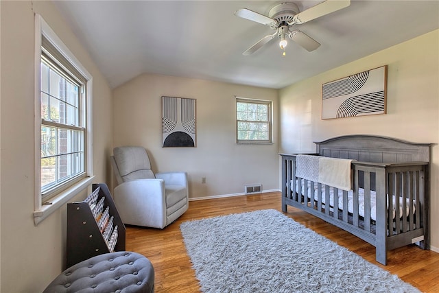 bedroom with wood-type flooring, vaulted ceiling, ceiling fan, and a crib