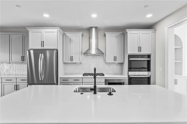 kitchen with sink, wall chimney range hood, stainless steel appliances, backsplash, and light stone countertops