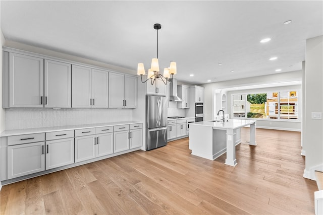 kitchen featuring light hardwood / wood-style floors, sink, an island with sink, wall chimney exhaust hood, and stainless steel fridge