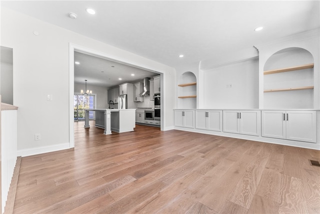 unfurnished living room with light hardwood / wood-style floors, an inviting chandelier, sink, and built in shelves