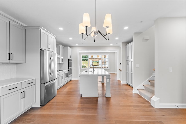 kitchen with sink, decorative light fixtures, light hardwood / wood-style flooring, stainless steel appliances, and an inviting chandelier