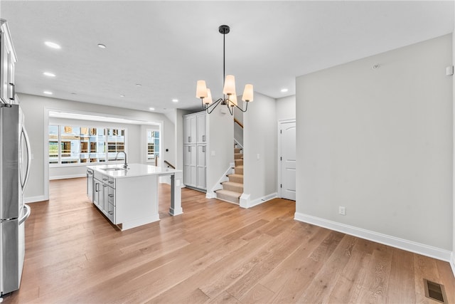 kitchen featuring an island with sink, white cabinets, pendant lighting, light hardwood / wood-style flooring, and sink