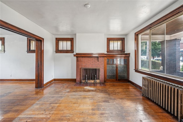 unfurnished living room with hardwood / wood-style flooring, radiator, and a brick fireplace