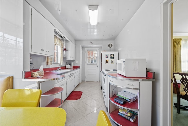 kitchen with a healthy amount of sunlight, light tile patterned flooring, white cabinetry, and electric range