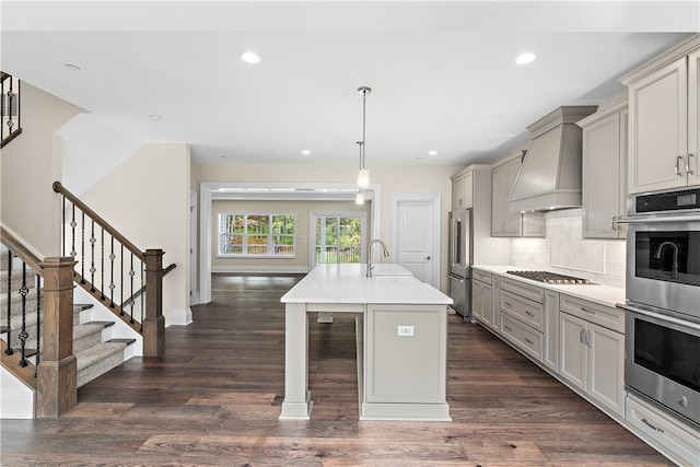 kitchen with an island with sink, stainless steel appliances, dark wood-type flooring, and custom exhaust hood