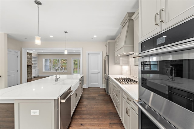 kitchen featuring pendant lighting, sink, a kitchen island with sink, dark wood-type flooring, and stainless steel appliances