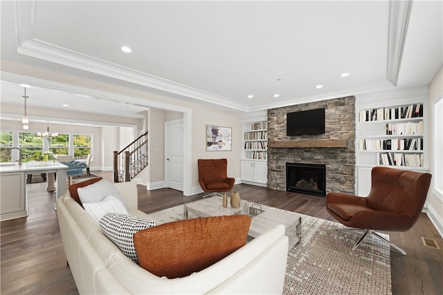 living room with a stone fireplace, crown molding, dark hardwood / wood-style flooring, and built in features