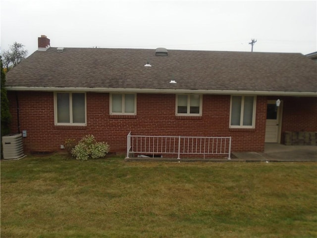 rear view of house featuring a lawn, a chimney, brick siding, and central air condition unit